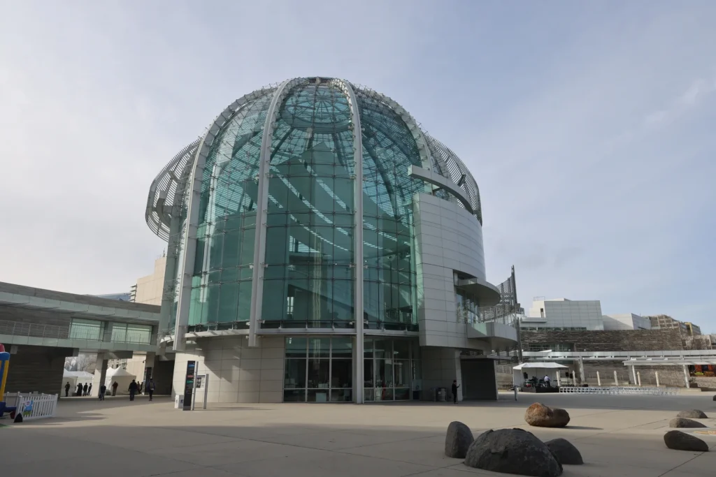 Large building with a glass dome on top of it, surrounded by a group of people standing on the ground