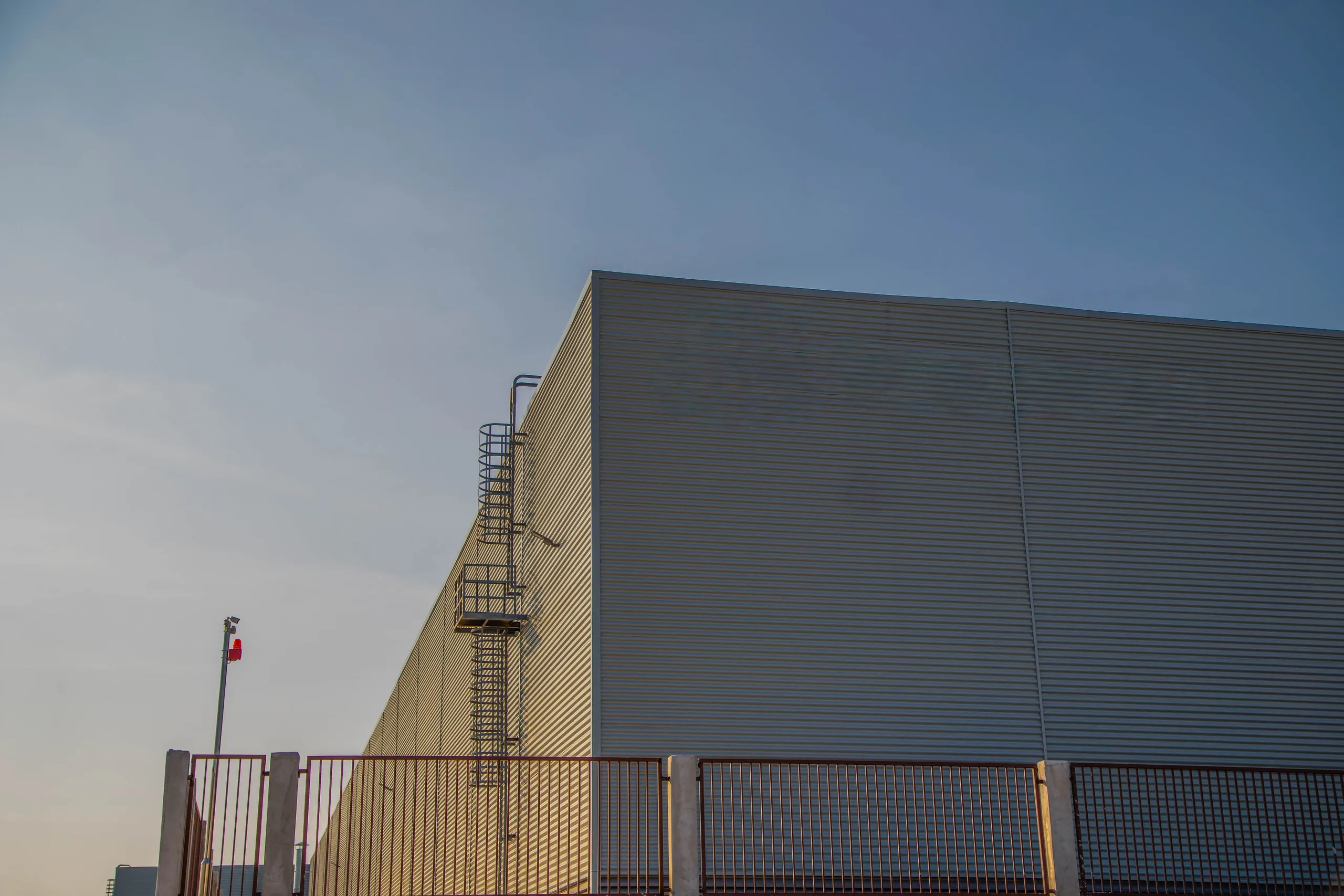 Large building with a metal fence in front of it, a metal gate, a pole with a flag
