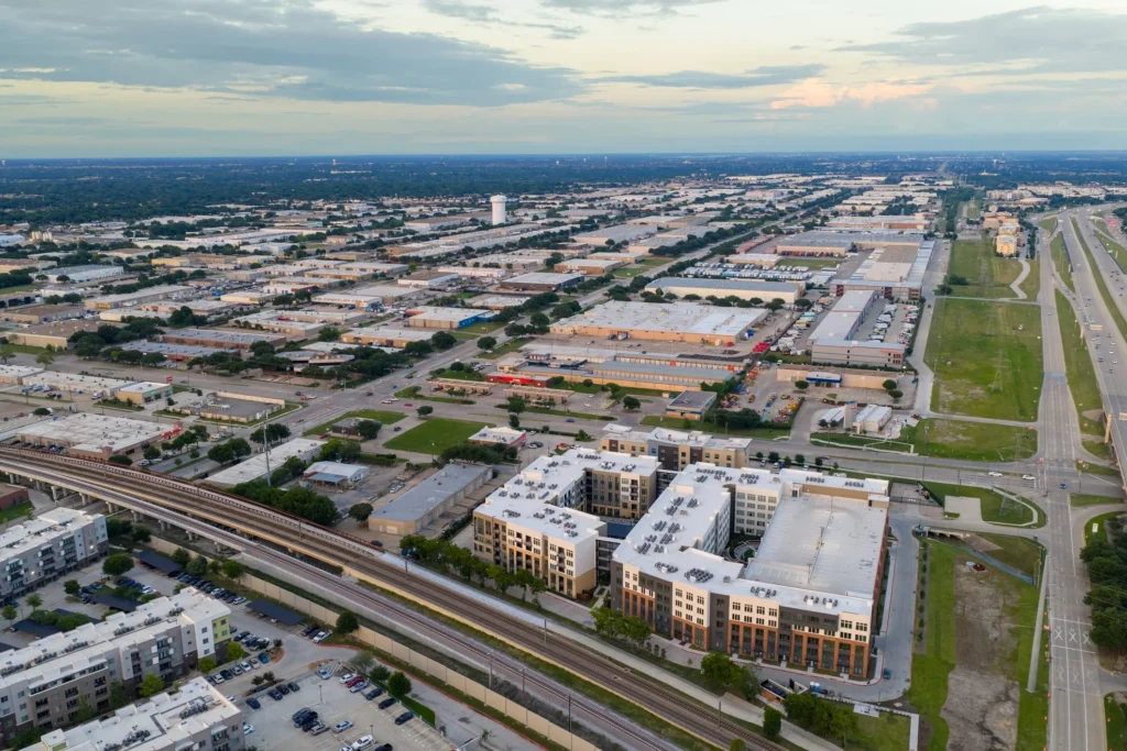 Aerial view of a city with lots of buildings, trees, roads, vehicles, grass, poles, and a bridge