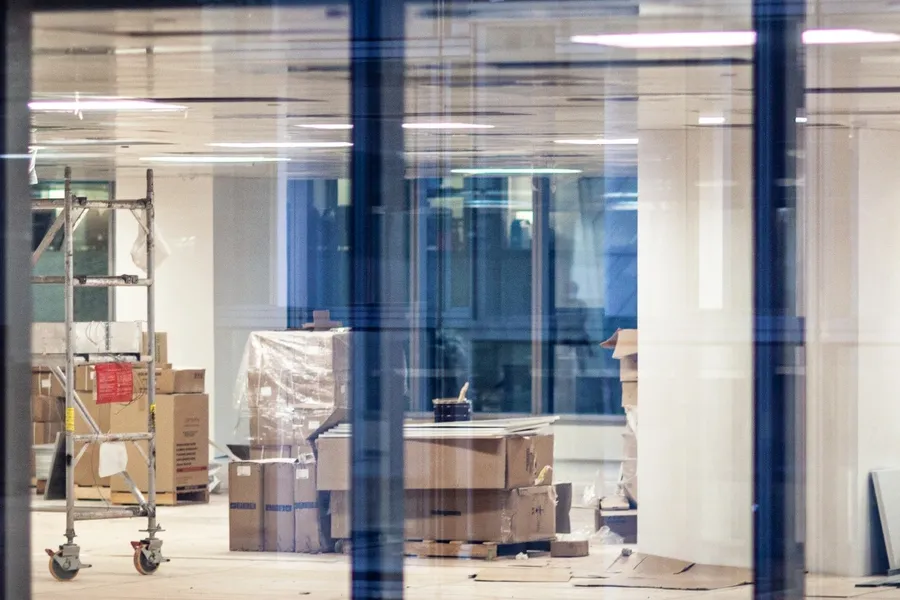 Large room filled with lots of cardboard boxes and a ladder, as well as glass doors, walls