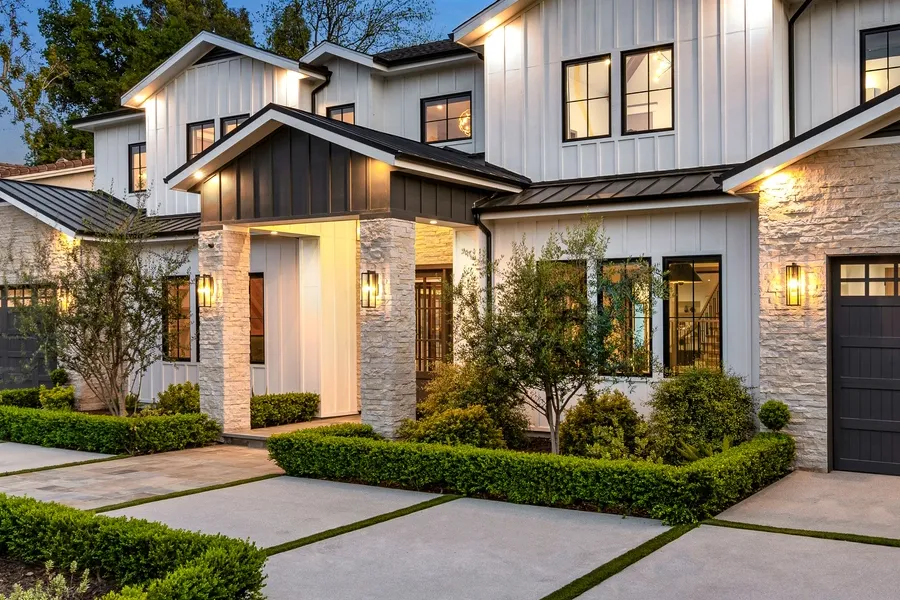 Modern house with a driveway in front of it, surrounded by trees, plants, and grass