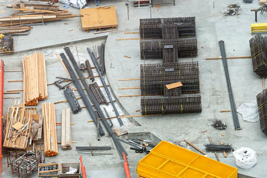 Aerial view of a construction site with a large pile of construction materials, including iron rods, wooden planks