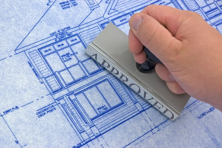 Person's hand holding a rubber stamp over a blueprint of a house, likely for a home inspection