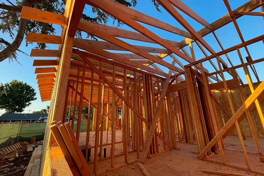 House under construction with a lot of wood framing, surrounded by trees, houses, and a fence