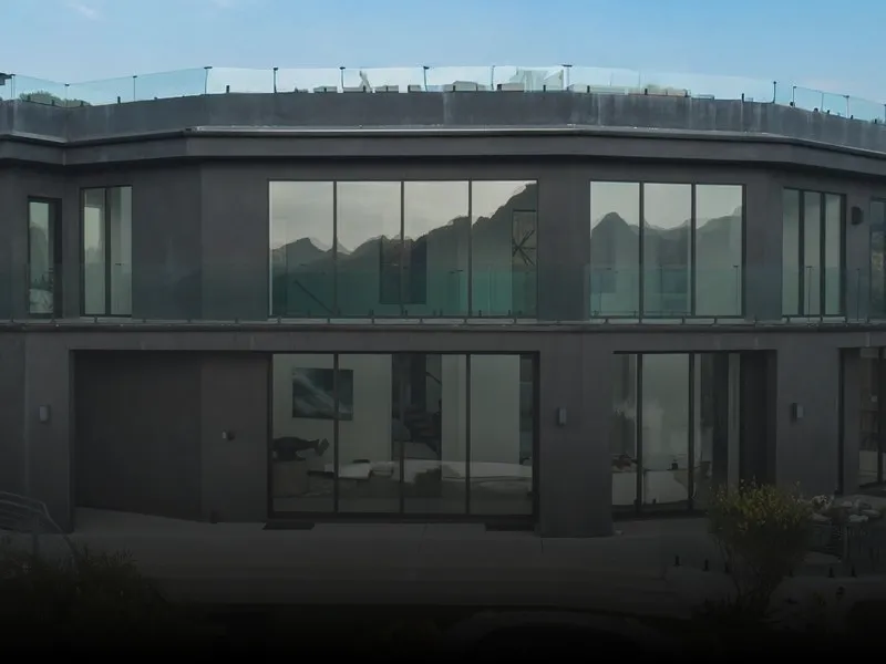 Large building with glass walls and a glass railing, surrounded by lush plants